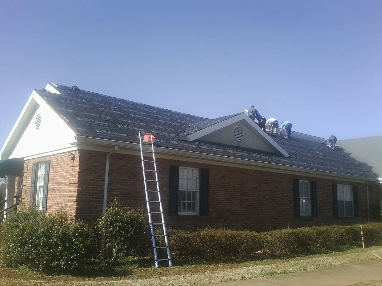 Crew tearing shingles off a brick ranch roof with a ladder set — Metal Roof Repair work by our crew in Willernie