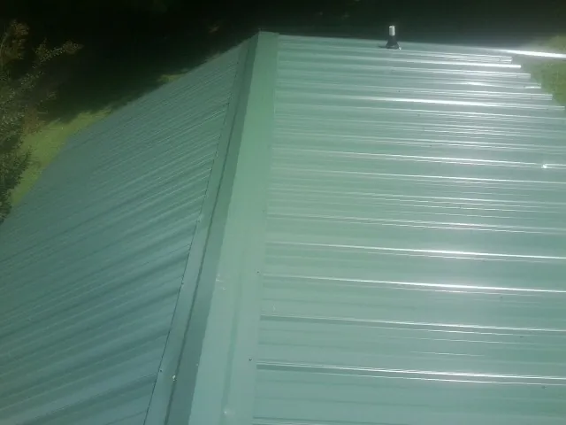 New green metal panels meeting at the ridge of a roof — Flat Roof Repair work by our crew in Willernie