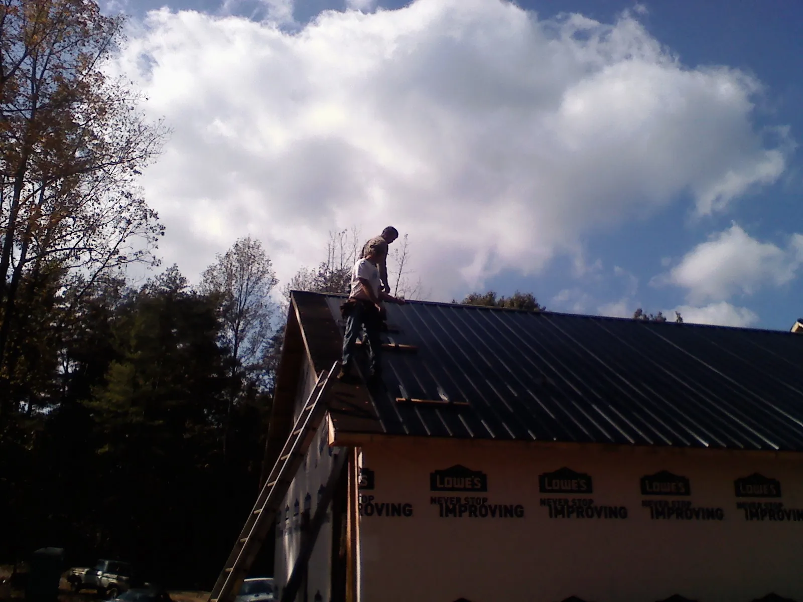 Roofer fastening dark metal panels high against a cloudy sky, from a Roof Inspection job in Willernie
